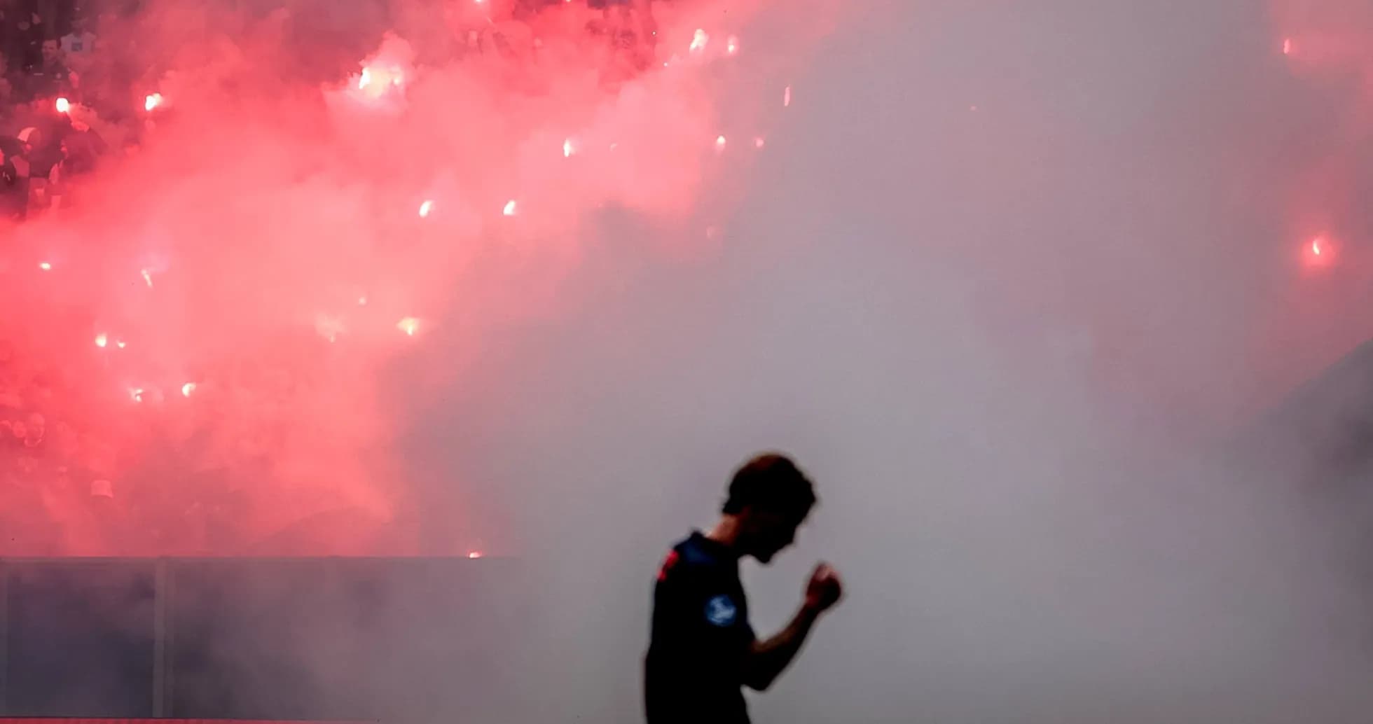 Jugador caminando entre humo y bengalas en estadio