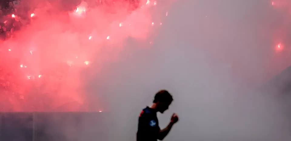 Jugador caminando entre humo y bengalas en estadio