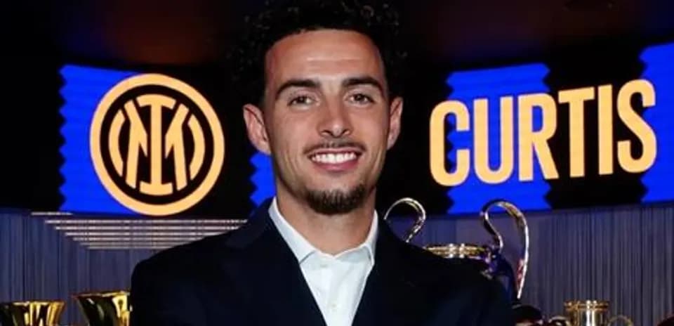 Jugador sonriendo en evento con trofeos detrás