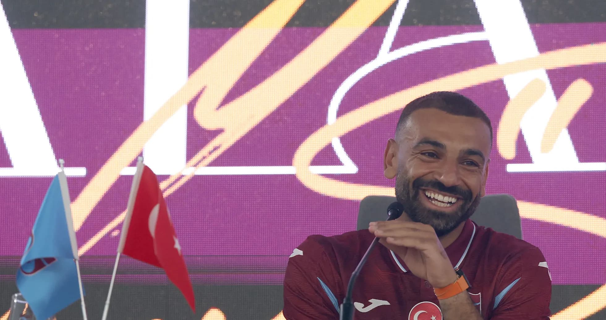 Jugador sonriendo en conferencia de prensa con banderas