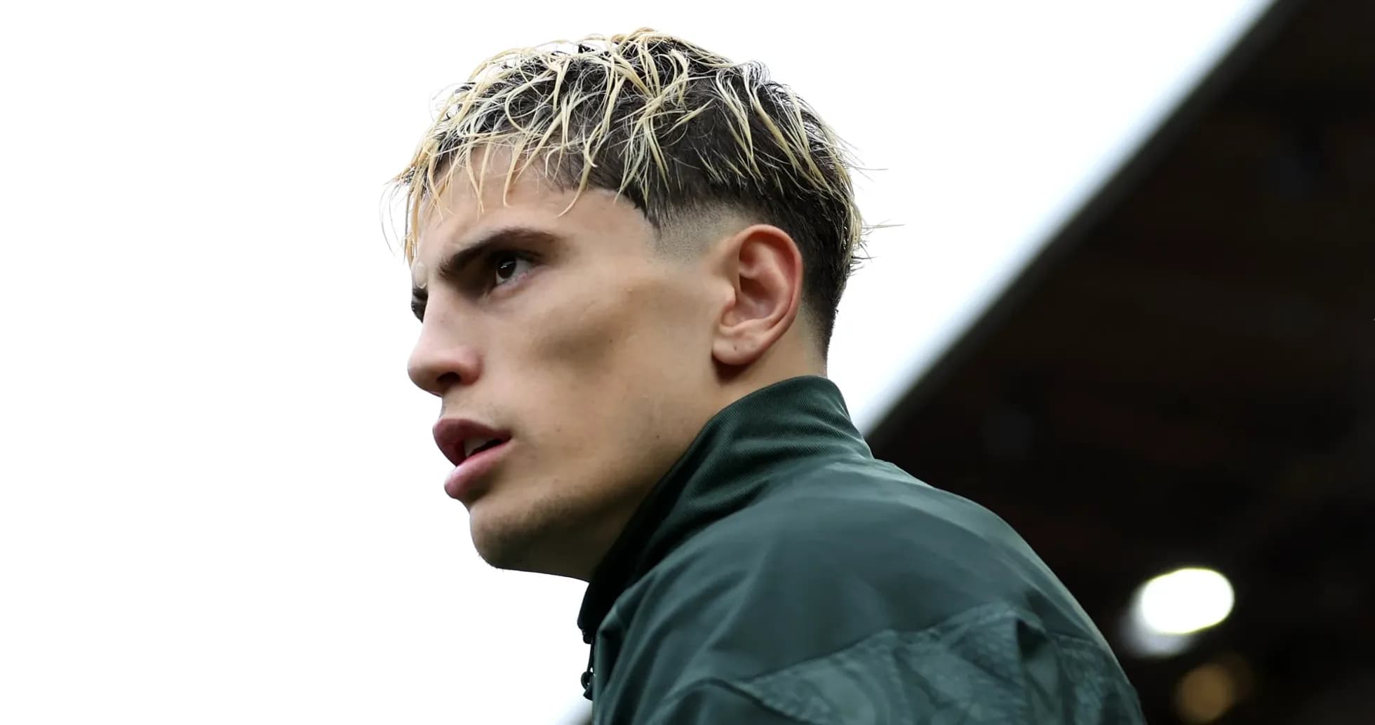 Jugador en perfil con cabello rubio y chaqueta verde
