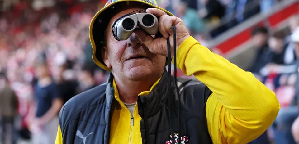 A fan wearing binoculars and a yellow hat