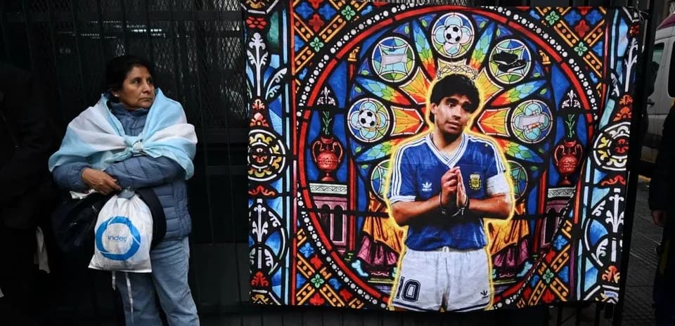 Mujer con bandera argentina frente a mural de Maradona