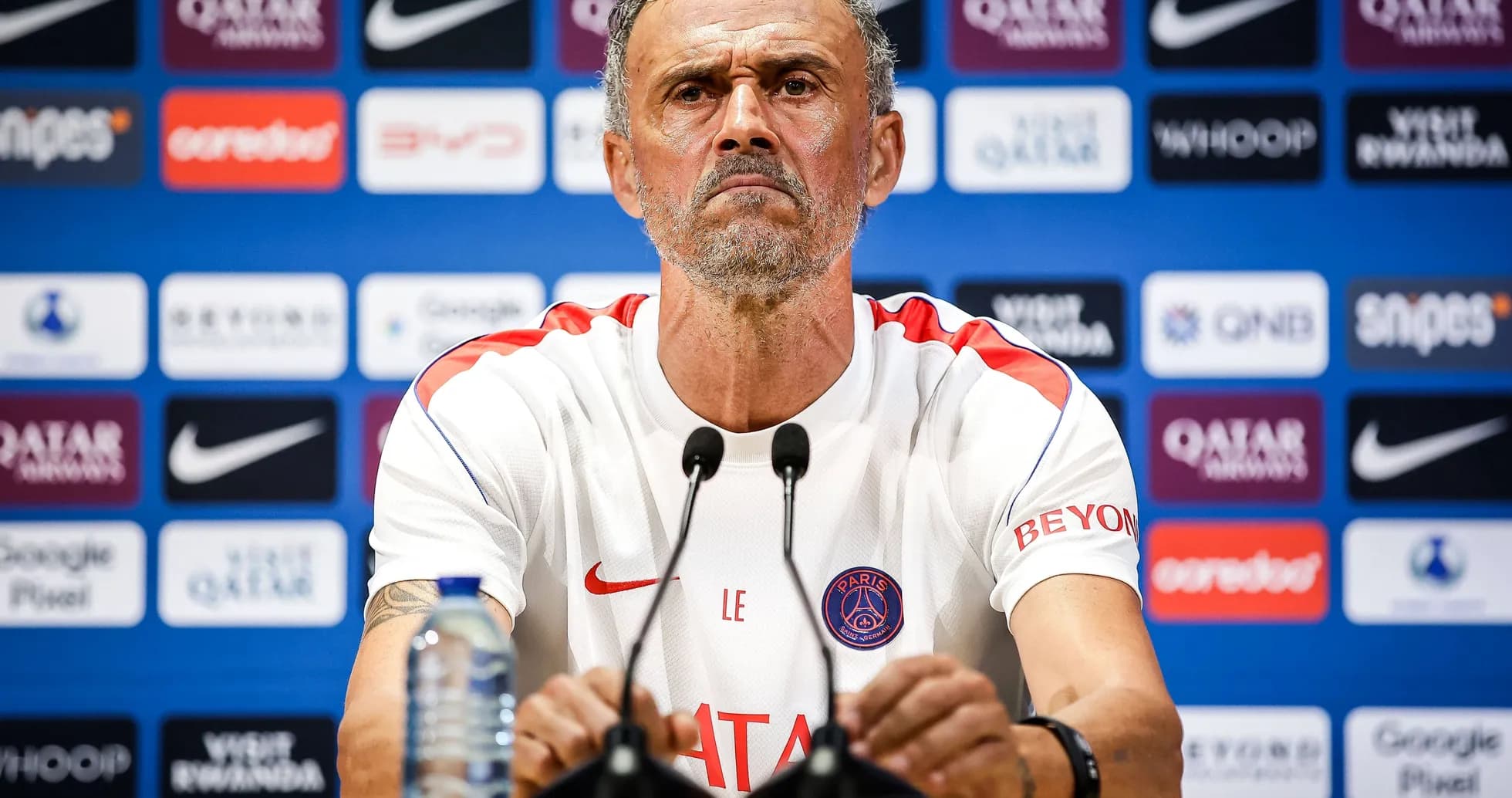 Entrenador en rueda de prensa con logotipo del PSG