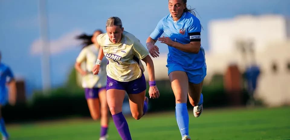 Jugadora de JMU corriendo con balón, seguida por rival