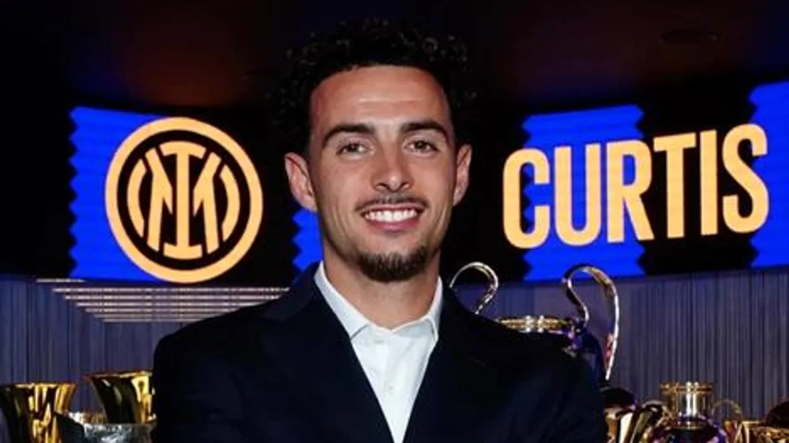 Jugador sonriendo en evento con trofeos detrás Jugador sonriendo en evento con trofeos detrás