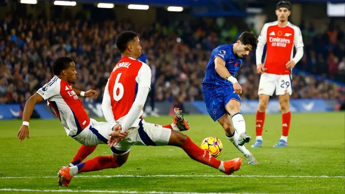 Jugador de Chelsea disparando mientras dos defensores de Arsenal intentan interceptar Jugador de Chelsea disparando mientras dos defensores de Arsenal intentan interceptar