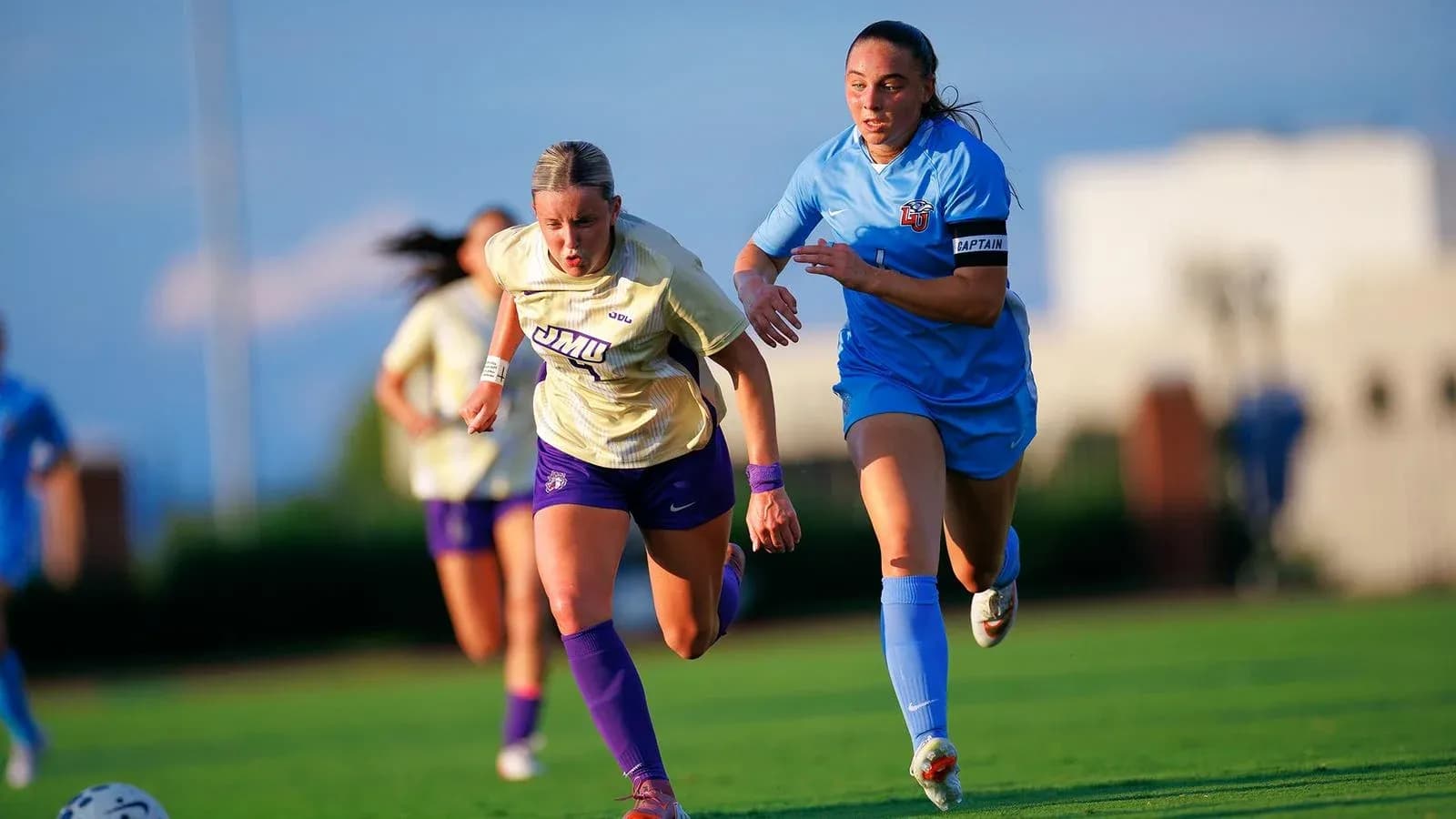 Jugadora de JMU corriendo con balón, seguida por rival Jugadora de JMU corriendo con balón, seguida por rival